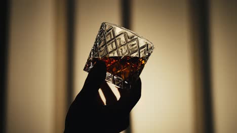 slow motion shot of a hand swirling a glass of bourbon whiskey back lit