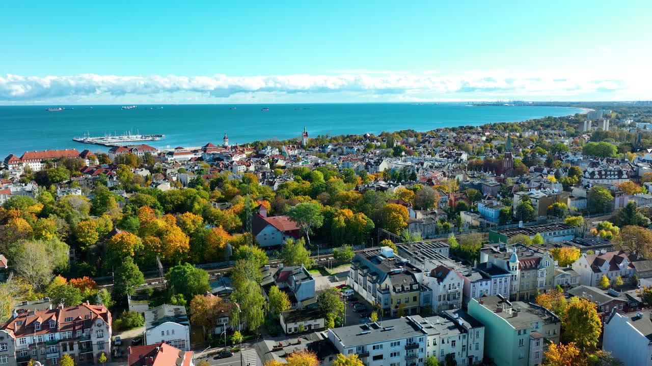 Drone view of Sopot showing historic city center, colorful trees, and Baltic Sea horizon