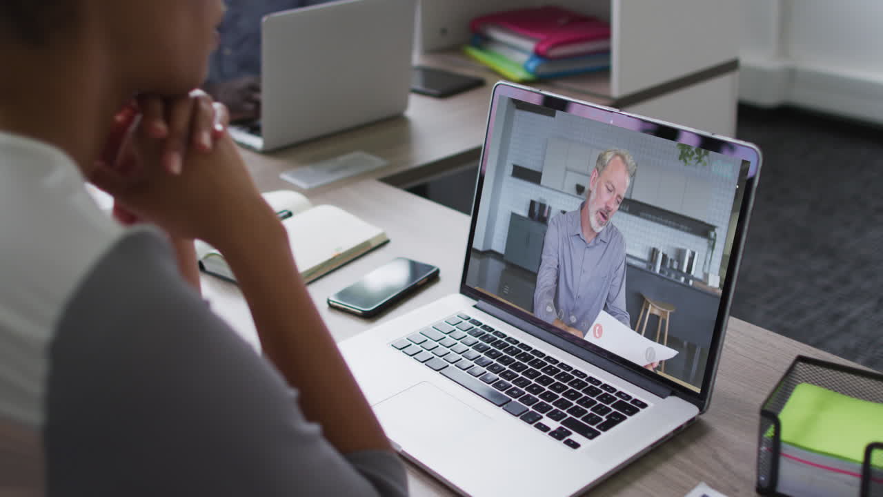 African american businesswoman sitting at desk using laptop having video call with male colleague