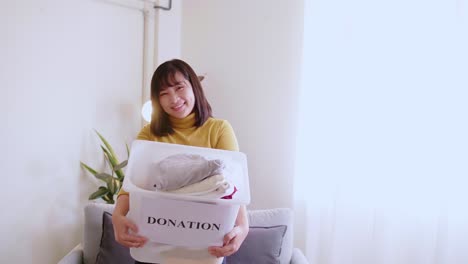 portrait of young pretty woman looking at camera holding box with clothes for donation