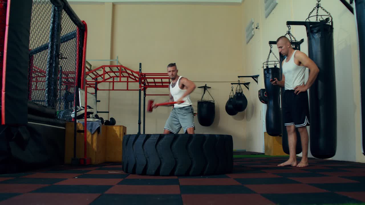 Spor salonunda kızak çekici ve lastikle egzersiz yapan adamlar