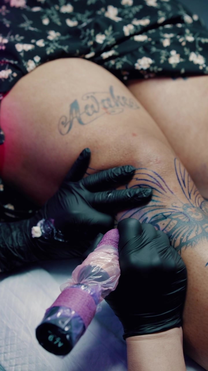 Tatuatore al lavoro su un tatuaggio alla gamba in uno studio