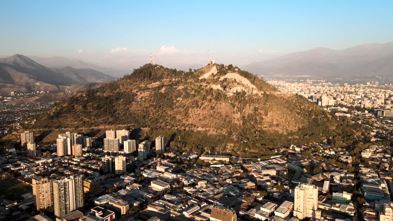 carretilla aérea en el cerro san cristobal que revela el horizonte de la ciudad de santiago y los edificios del vecindario rodeados de montes al atardecer, chile