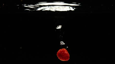 super slow motion of falling fresh raspberries into water on black background