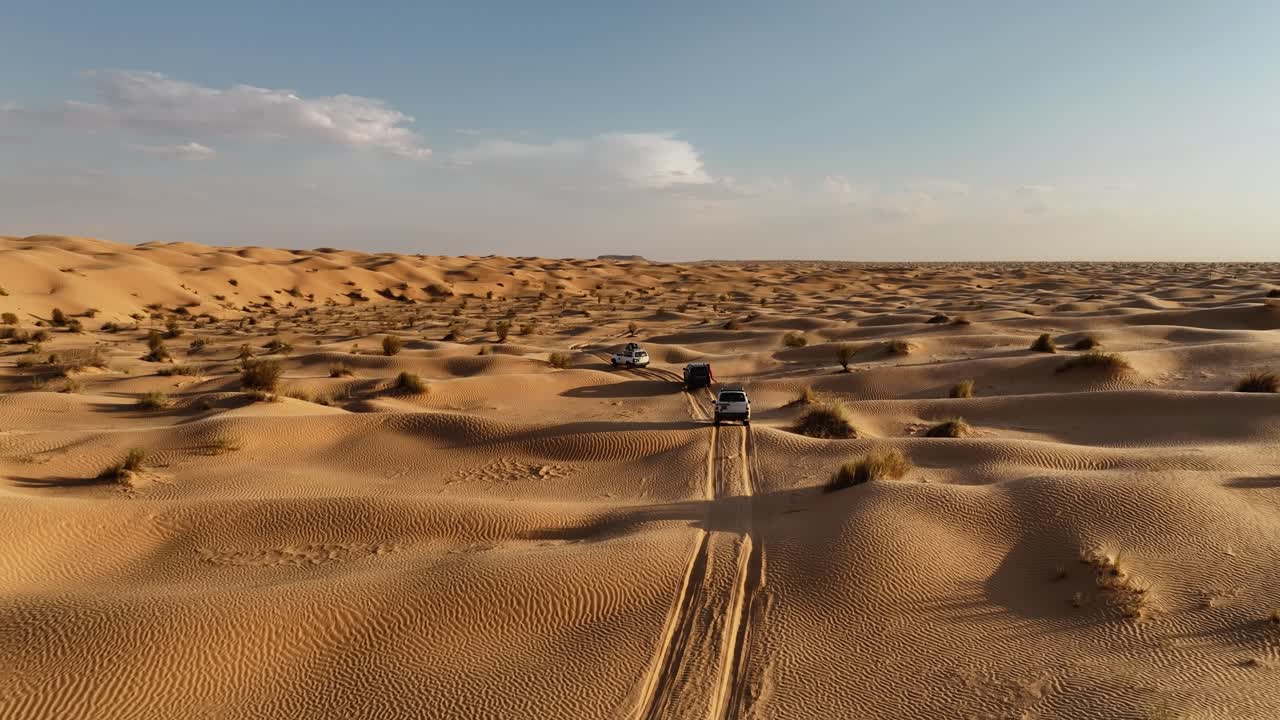 Il drone vola in alto osservando tre auto che attraversano il deserto del Sahara in Tunisia. Riprese aeree 4K.