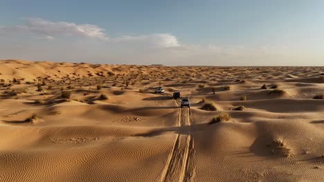 the drone is flying up looking at three cars driving through the sahara desert in tunisia aerial footage 4k