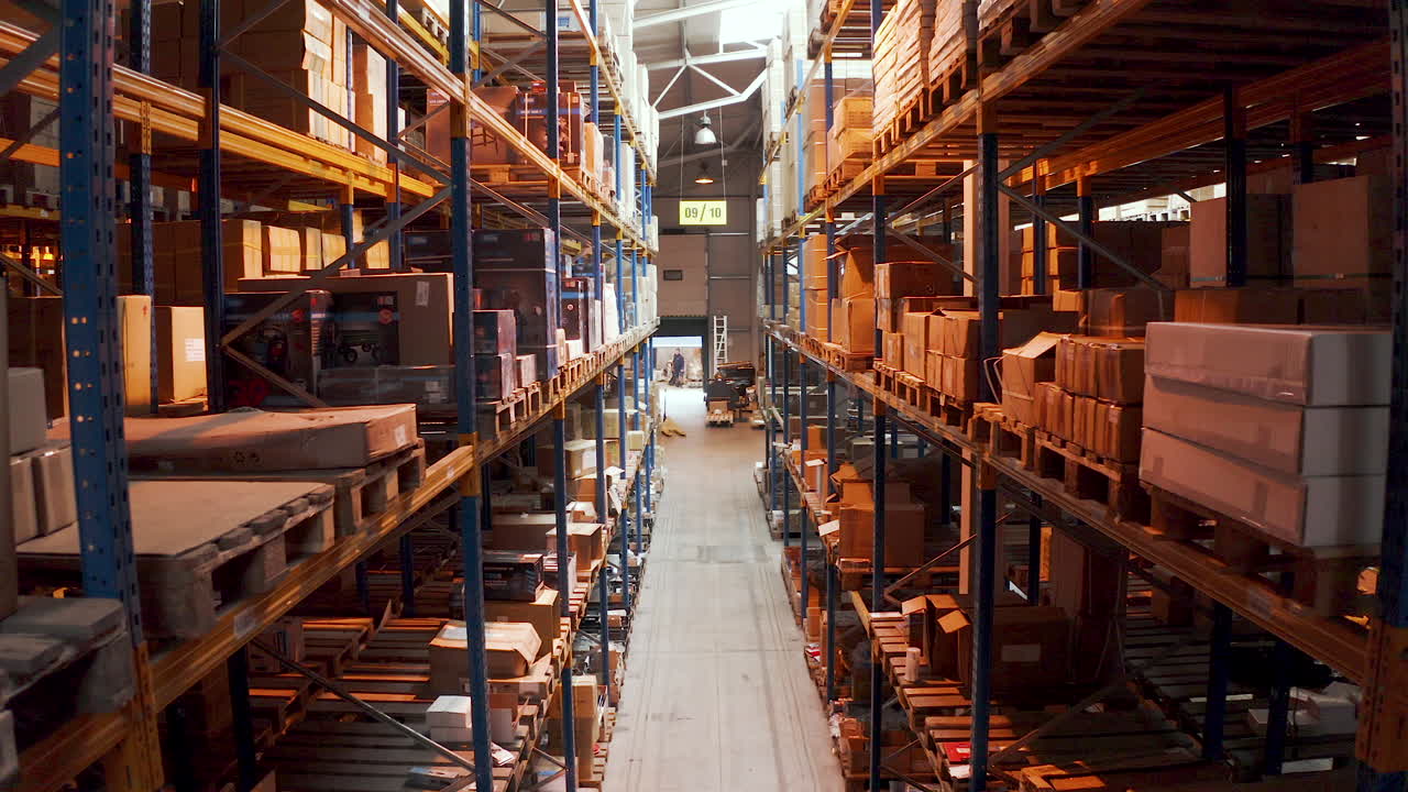 Man leaving a long warehouse aisle with stacked packed boxes,aerial