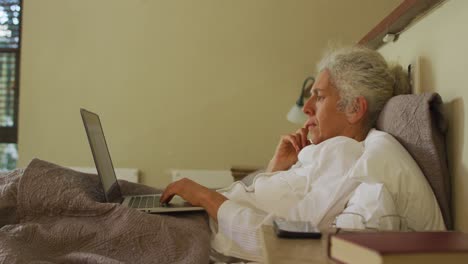 mujer de raza mixta mayor acostada en la cama usando una computadora portátil