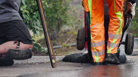 road workers dumping the tar or asphalt from the wheelbarrow on a working surface - closeup