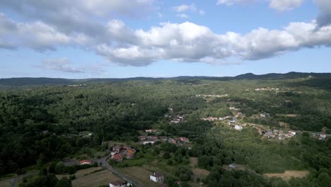 Drone-push-in-with-spanish-rural-small-town-village-nestled-in-forest,-cloudy-sky-day