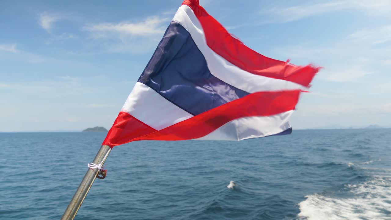 Thailand flag waving at the back of a ferry boat cutting through the clear waters of the Andaman Sea