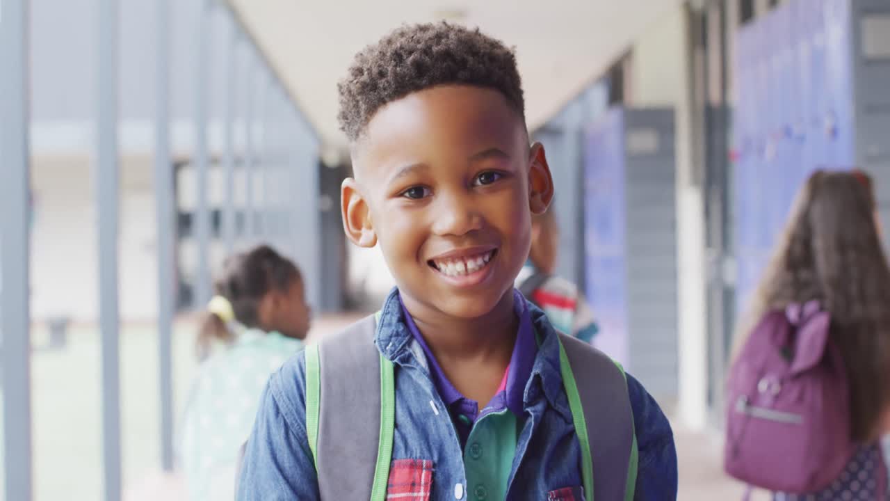 Ritratto di scolaro afroamericano felice che cammina nel corridoio della scuola.