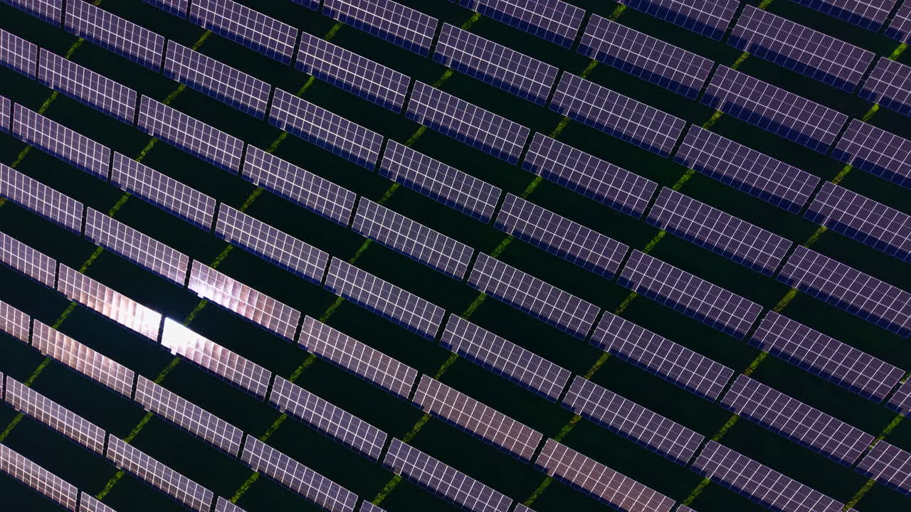 Ampio impianto fotovoltaico che cattura la luce solare su un paesaggio verde sotto un cielo azzurro e limpido a mezzogiorno.