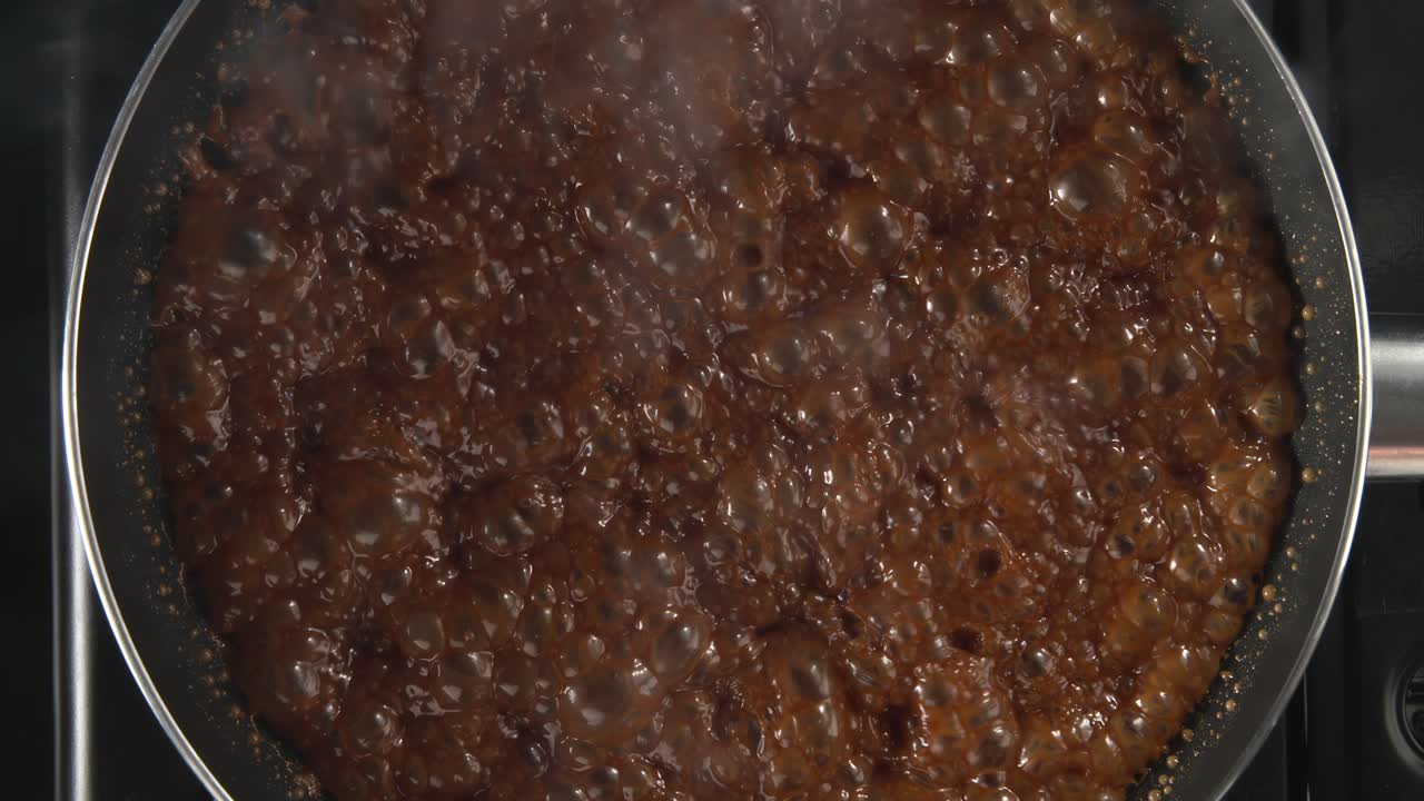 el azúcar derretido está hirviendo en el recipiente de metal en la estufa caliente, haciendo helado con plátano caramelizado, video de mesa 4k