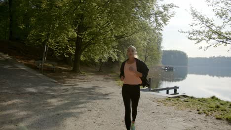 Runner-running-on-lakeside-near-woods-on-sunny-day