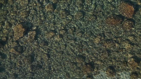 drone top down bird's eye view of shimmering light ripples dancing across rocky boulders below water