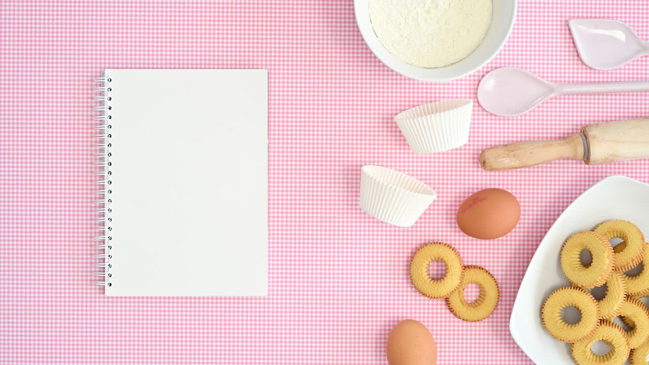 mover comestibles de horneado y galletas frescas en tema rosa pastel con cuaderno abierto para recetas. detener el movimiento de colocación plana