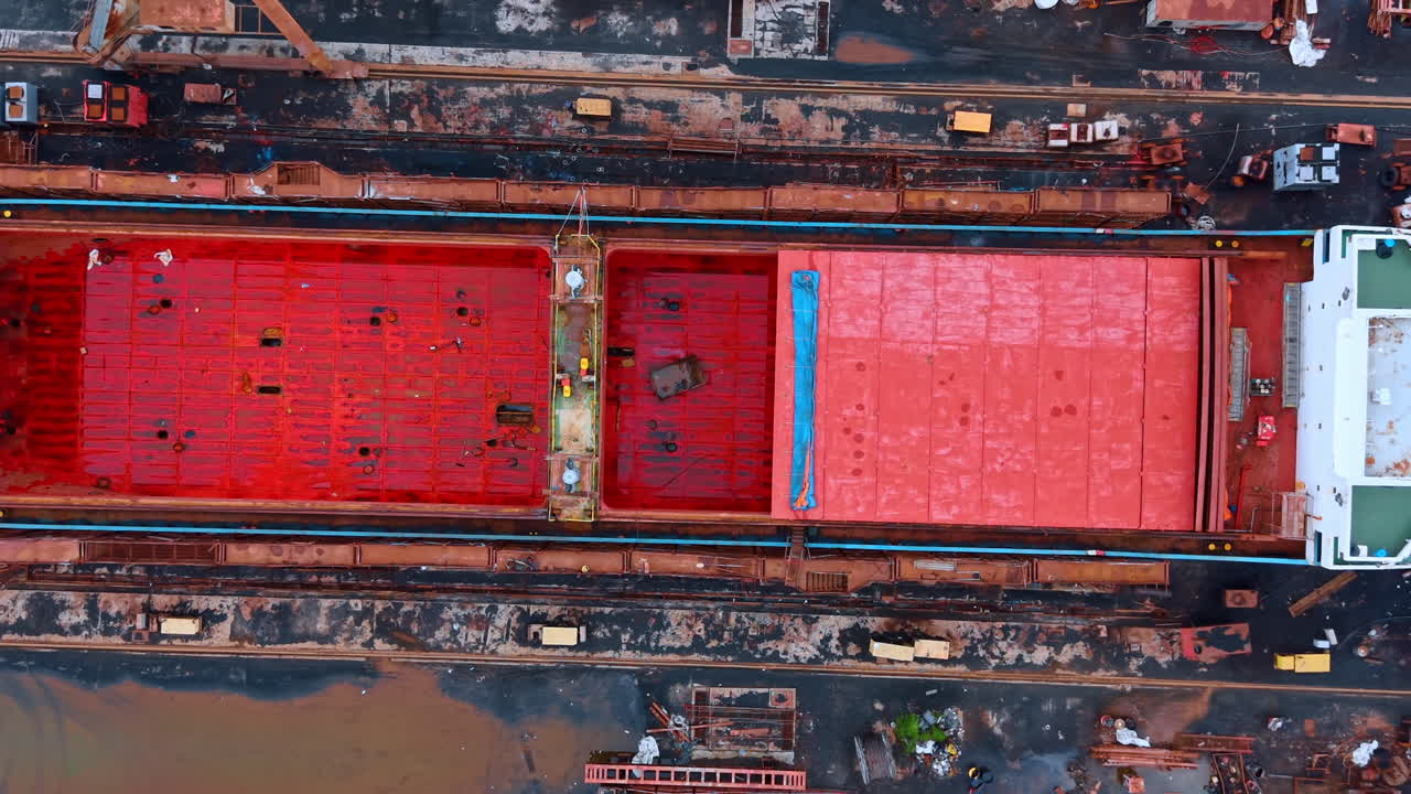 Top down view of cargo ship with red hatches. Vessel deck showing red cargo hold covers and green bridge
