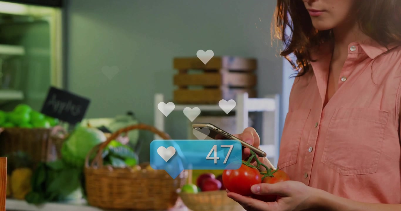 Creador tomando el teléfono y rastreando iconos de corazón ascendentes alrededor de tomates para retroalimentación en redes sociales.