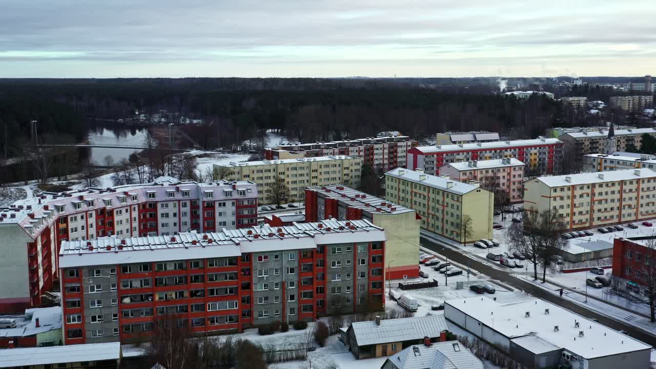 Talvinen kaupunkikuva, jossa on kerrostaloja, katu ja parkkipaikka lumipeitteisine autoineen ilmakuvassa yläviistosta kuvattuna