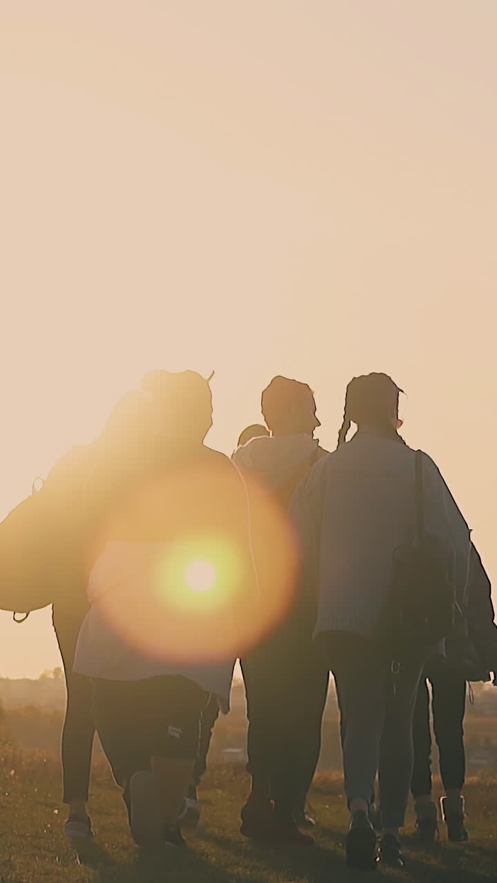 people silhouettes walk along meadow with dry grass against back rising sun in early autumn morning slow motion