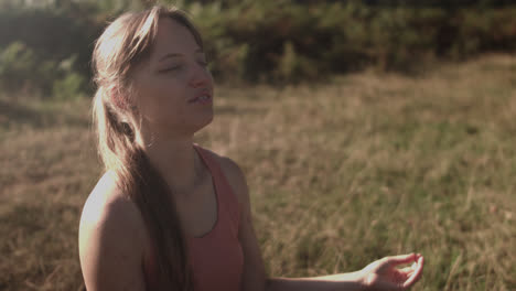 Woman-doing-namaste-while-sitting-in-the-park's-grass-and-meditating-while-taking-deep-breaths