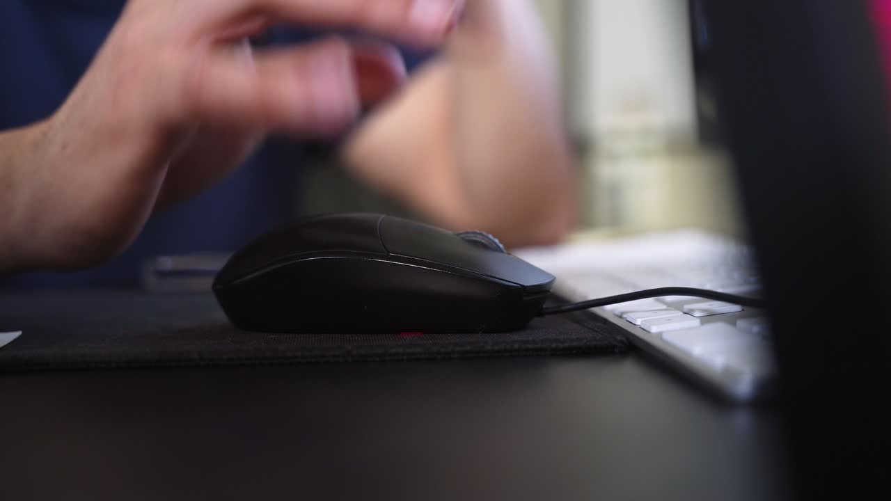 a hand using a computer mouse beside a keyboard on a modern desk, captured indoors with soft lighting and shallow depth of field in a workspace setting