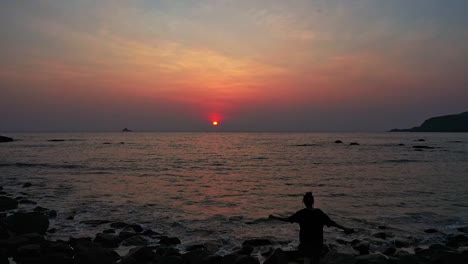girl is walking on the rocky shore of goa beach with dramatic sunset sky in india