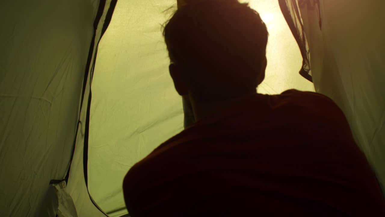 Young man backpacker exits camping tent in front of roman aqueduct arches in parco degli acquedotti park ruins in rome at sunset sticks in ground shot from inside tent camera slow motion pov