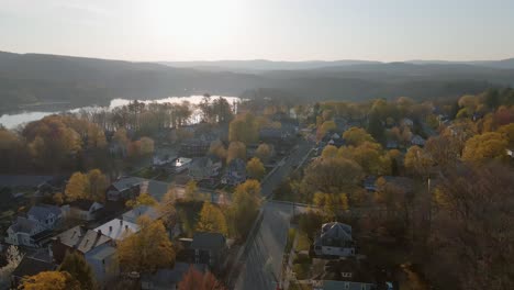 aerial take-off from the ground to the sunny autumn sky featuring a beautiful suburban area during the fall time positioned next to a big lake