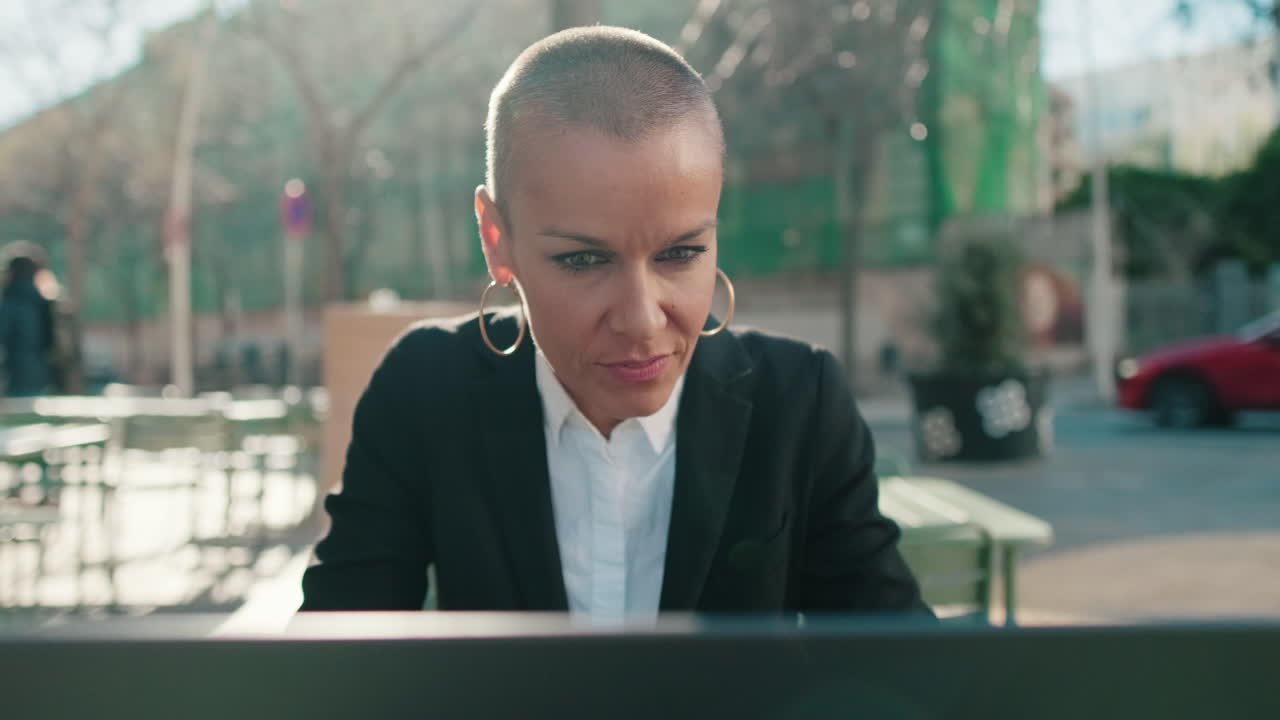 Confident Bald Woman Working on Laptop Outdoors Looks Up and Smiles