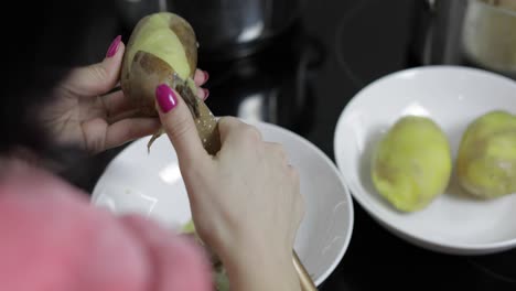 las manos de la ama de casa pelando patatas en la cocina.
