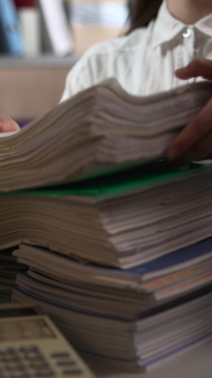 A metal office shelf holds stacked paper files and binders, with a telephone in the foreground and a blurred person working in the background under soft