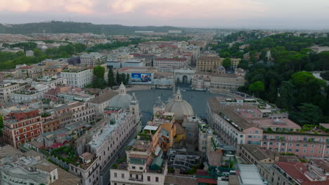 Elevated-view-of-oval-square-Piazza-del-Popolo-with-Egyptian-obelisk-in-middle.-Fly-above-buildings-in-historic-urban-borough-at-twilight.-Rome,-Italy