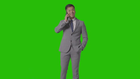 three quarter length studio shot of smiling businessman in suit talking on mobile phone against green screen