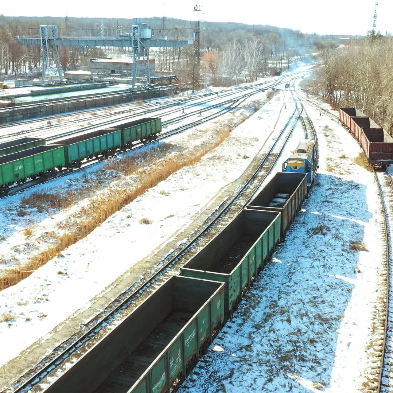 A freight train with containers moves along the rails in the direction of the city in a winter day. Shipping of goods. Aerial view.