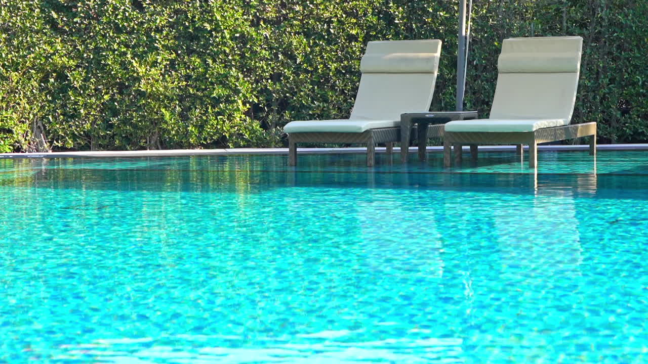To liggestole og et lille bord i lavt turkisblåt swimmingpoolvand på et tropisk hotelresort i Thailand