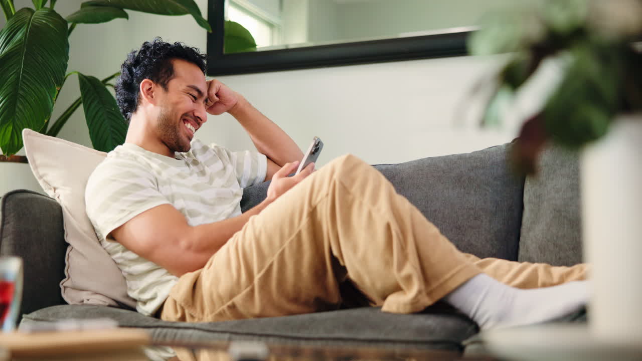 Giovane uomo che si rilassa sul divano e usa lo smartphone a casa.