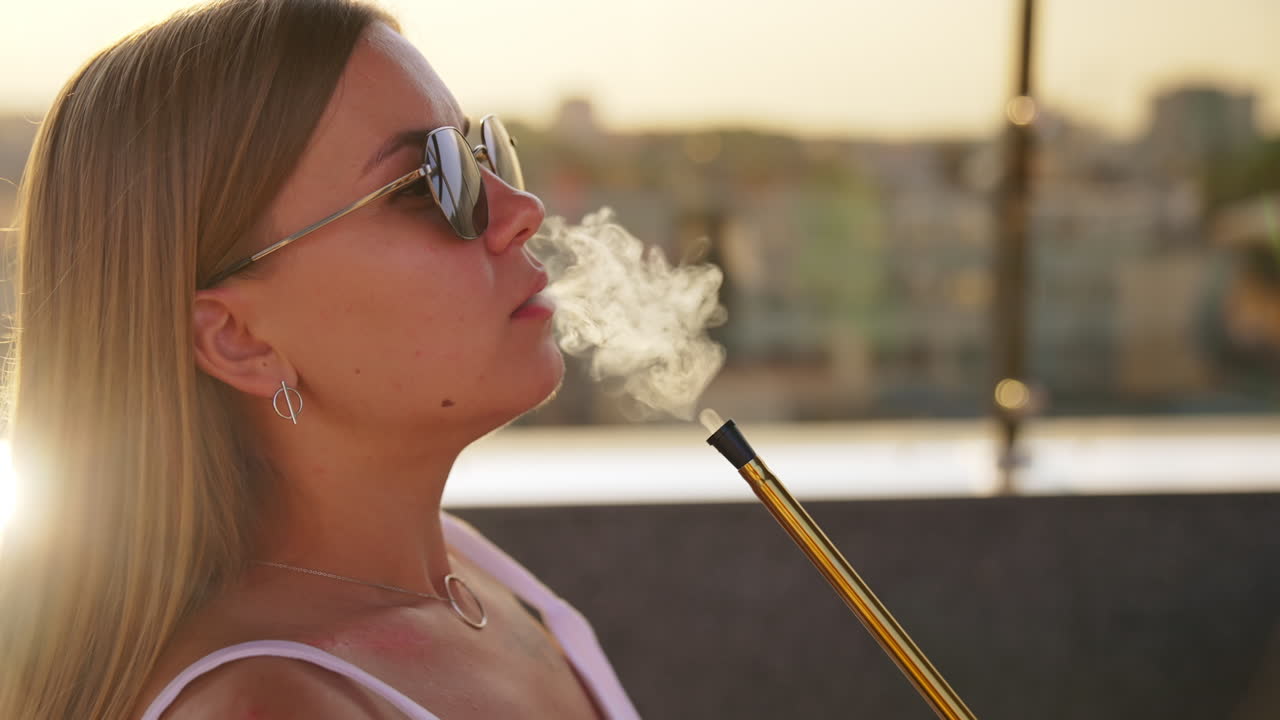 Smoking hookah in a café. Young long-haired woman breathes in and out thick white smoke. Close up. Blurred backdrop.