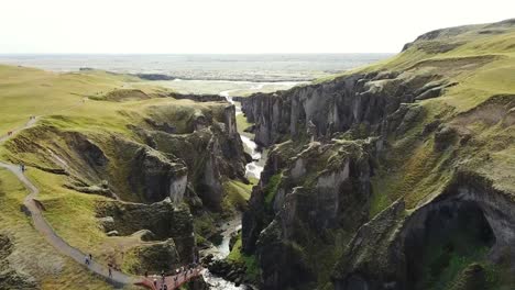 a stunning aerial view of fjaðrárgljúfur canyon featuring steep cliffs, winding pathways, and a flowing river amidst lush green landscapes. a captivating glimpse of iceland's natural beauty