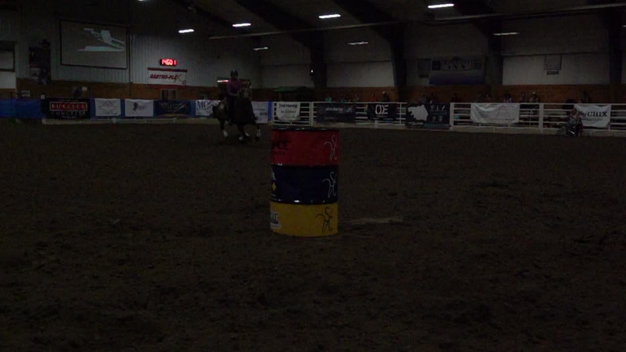 Cavaliere e cavallo che competono nella barrel race in un'arena al coperto