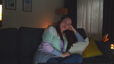 mujer sonriente sentada en el sofá en casa por la noche transmitiendo o viendo una película o un programa en la computadora portátil 7