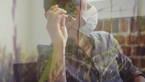 tall grass moving in the wind against caucasian man wearing face mask holding pen at office