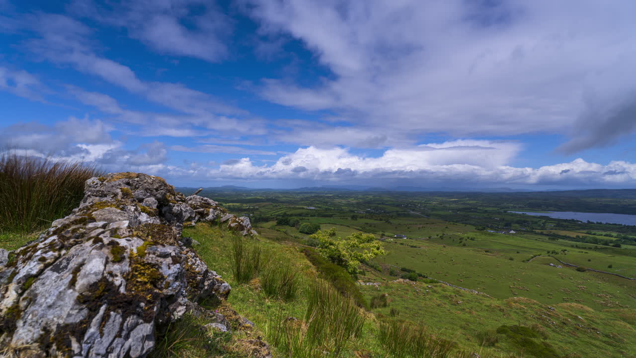 Timelapse af landligt landskab med klippeformation i forgrunden samt bakker og sø i det fjerne p en solrig, skyet dag set fra Carrowkeel i County Sligo i Irland