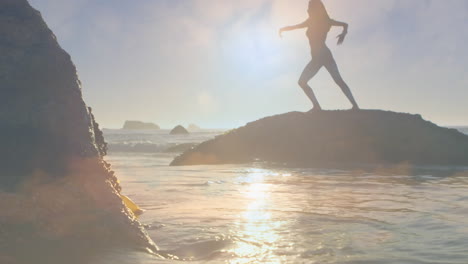 silhouette of woman practicing yoga standing on rock by seaside on sunny day