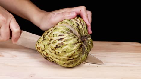 hands slicing a custard apple on table