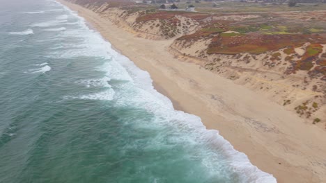 drone starts above ocean facing dunes, rotates and flies parallel to the beach, tracking coastline