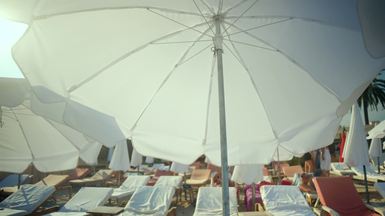 Bagnanti che si rilassano sotto ombrelloni bianchi e su lettini prendisole, godendosi una vacanza estiva in un resort durante una giornata di sole.