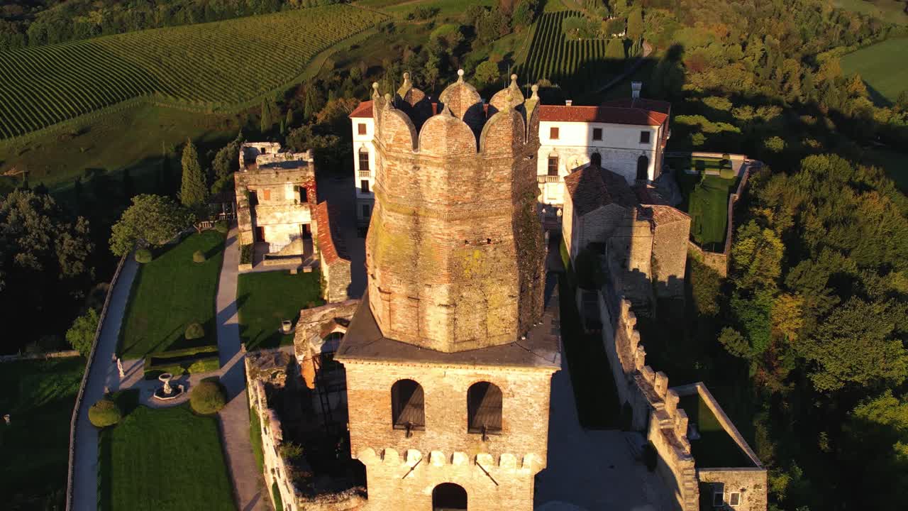vista aérea de un castillo medieval en la cima de una colina, rodeado de viñedos de prosecco, en italia