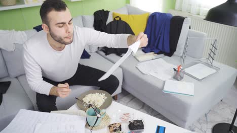 lazy man eating in his messy and dirty house, looking at paperwork.